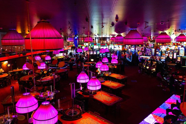 Interior de cassino moderno com mesas de jogos e caça-níqueis, iluminação colorida em tons de rosa e roxo, ambiente vibrante típico de cassinos internacionais