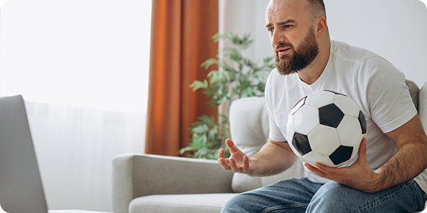 homem assistindo a uma partida no computador com uma bola na mão